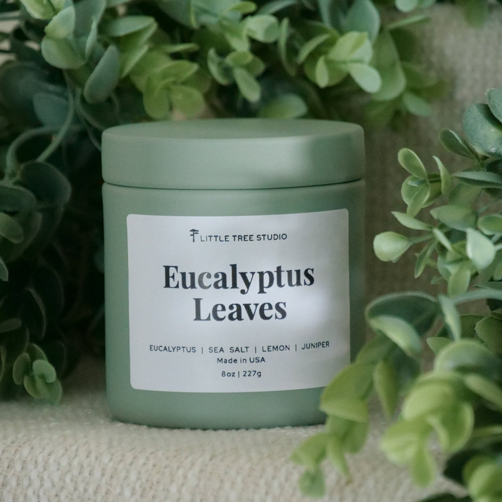 Green candle jar labeled 'Eucalyptus Leaves' by Little Tree Studio surrounded by greenery.